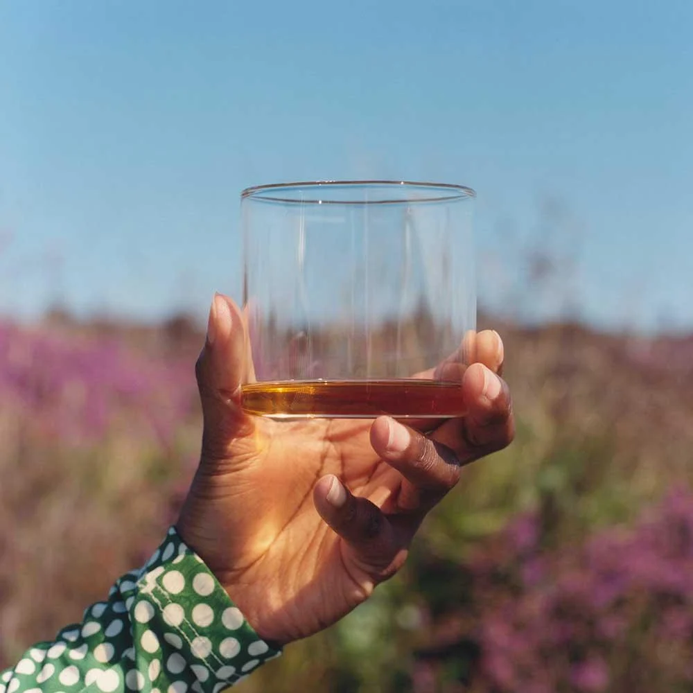 Una mano solleva un bicchiere di Highland Park 12 anni davanti a un campo di erica fiorita nelle isole Orcadi durante la degustazione.