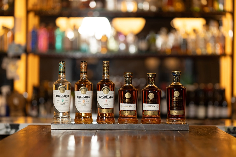 Selezione di rum Angostura allineata sul bancone in legno di un cocktail bar - Bottiglie per miscelazione e degustazione slow drinking