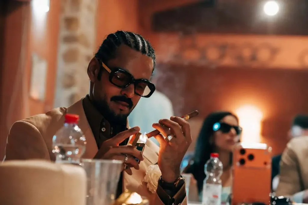 Jasim Hamed in abito elegante accende con cura un sigaro Havana durante i panel del XX Amigos de Partagás 2026.