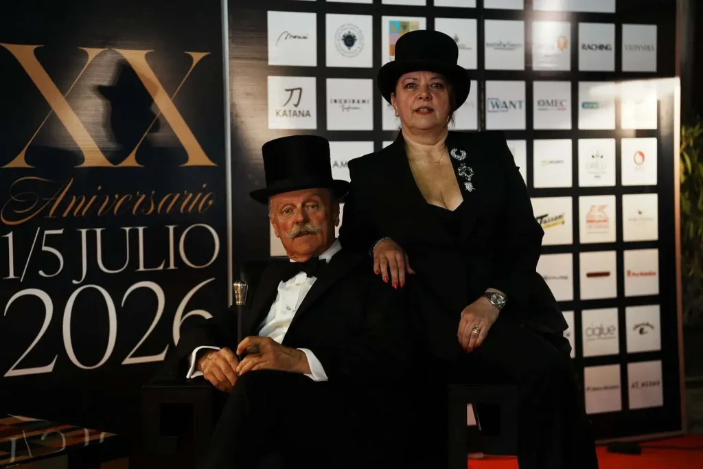 Bruno Ilari e Fiorella Palazzi in cappello a cilindro ed eleganza classica davanti al wall ufficiale del XX Amigos de Partagás 2026