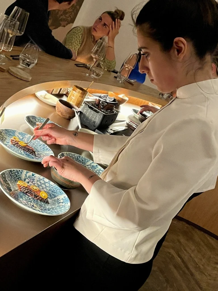 La Chef Pasticcera Matilde Pangrazi concentrata al bancone mentre rifinisce con le pinze i piatti della chiusura dolce da Akoya a Torino.