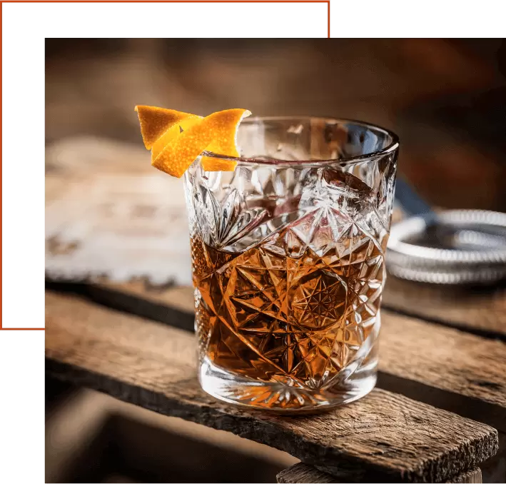 Bicchiere tumbler di cristallo con cocktail a base di Amaro Amara, ghiaccio e scorza d'arancia twist