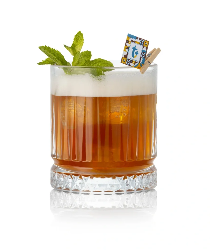 Bicchiere di cocktail Tea Sour preparato con T+ liquore al tè, schiuma e foglia di menta fresca