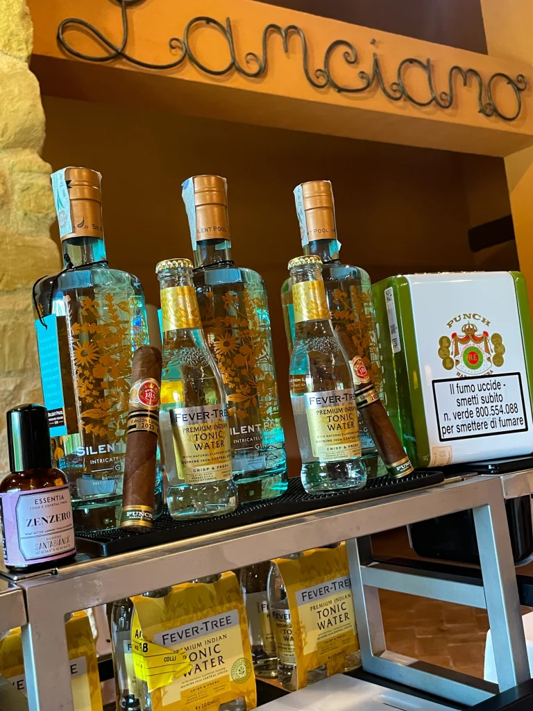 Un sigaro cubano appoggiato sul banco bar provvisto di bottiglie di Gin Silent Pool e acqua tonica Fever Tree per l'aperitivo firmato Velier