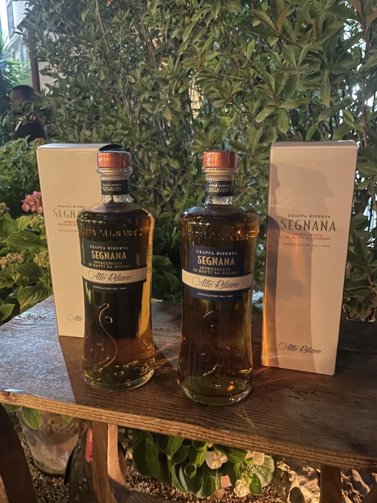 Due bottiglie di Grappa Riserva Segnana Alto Rilievo invecchiate in botti da Sherry e Whisky esposte su un tavolo di legno.