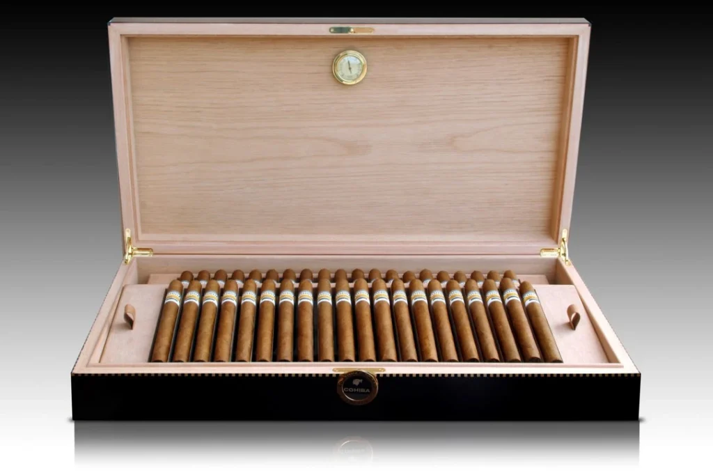 Elegante scatola humidor in legno aperta contenente una selezione di sigari premium Cohiba con igrometro sul coperchio.