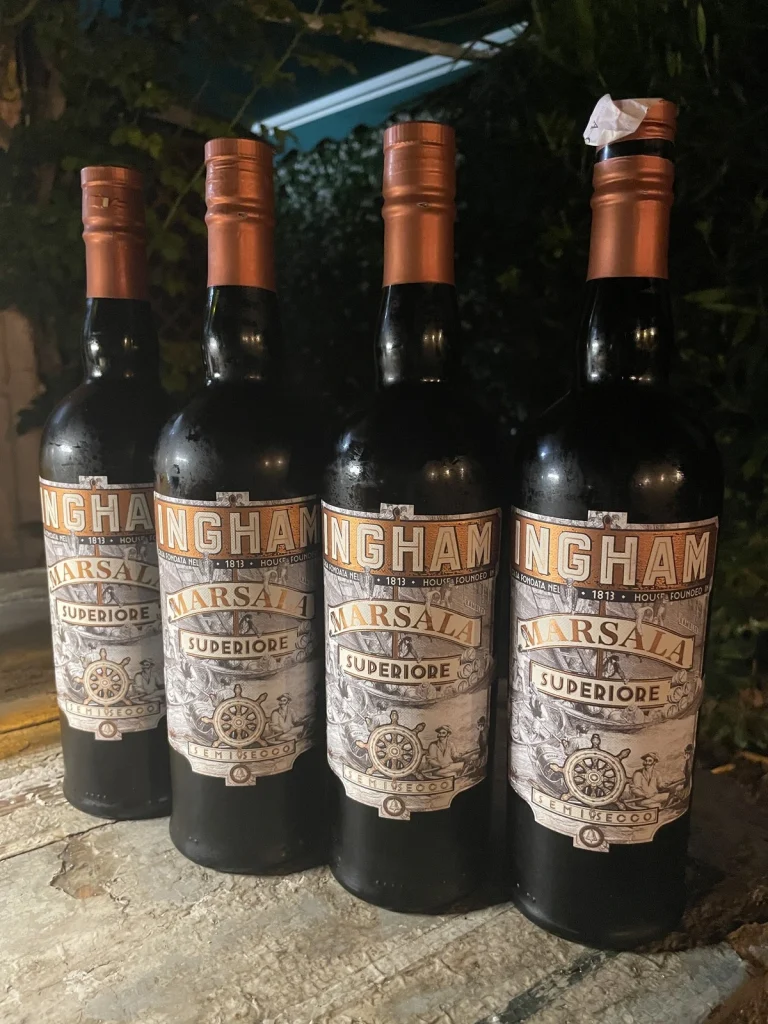 Quattro bottiglie di Marsala Superiore Ingham Semisecco allineate su un tavolo di legno all'aperto durante l'evento
