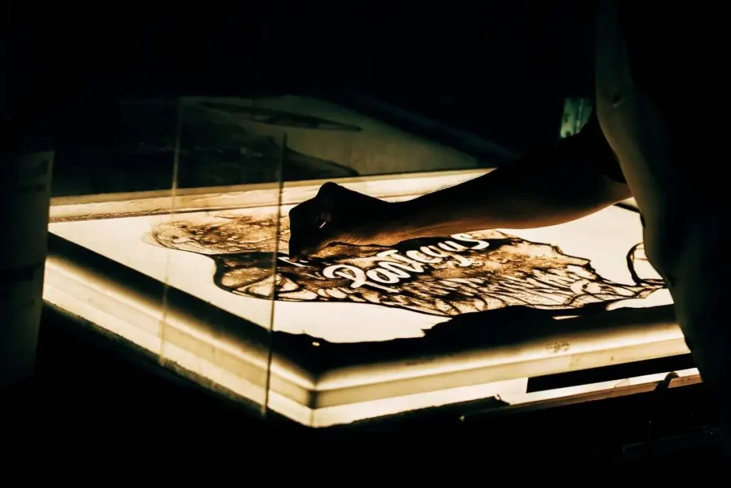 Dettaglio della mano dell'artista che realizza con la sabbia un disegno su un tavolo luminoso durante uno spettacolo dal vivo.