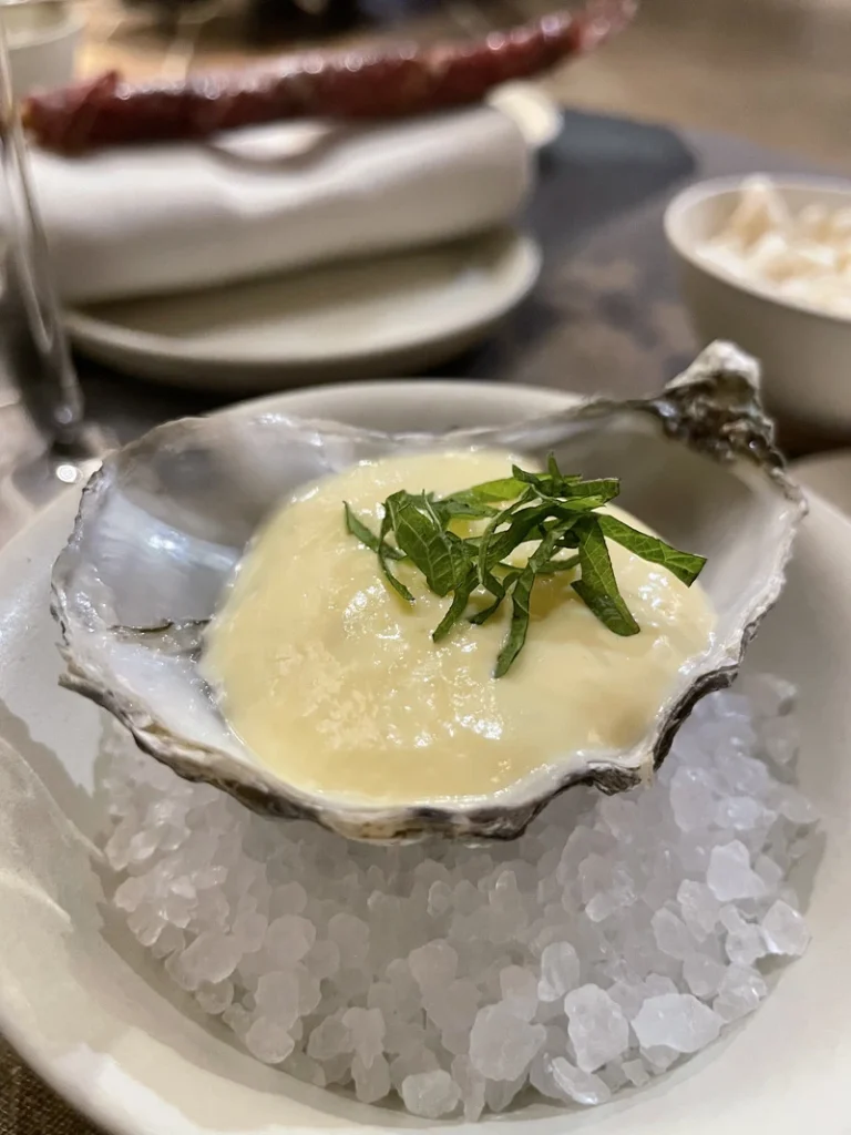Ostrica servita su un letto di sale grosso con emulsione e guarnizione di shiso, parte del menu degustazione del ristorante Akoya.