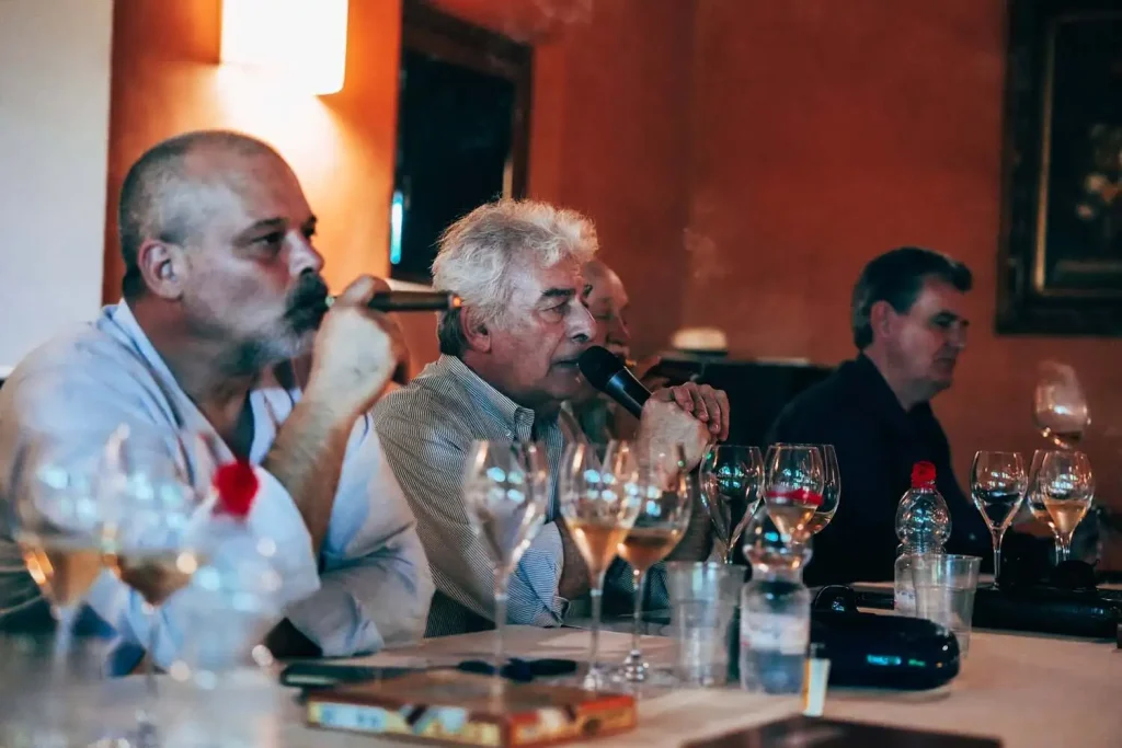 Il panel dei relatori al microfono mentre fuma ed effettua l'analisi sensoriale in abbinamento ai calici di vino.