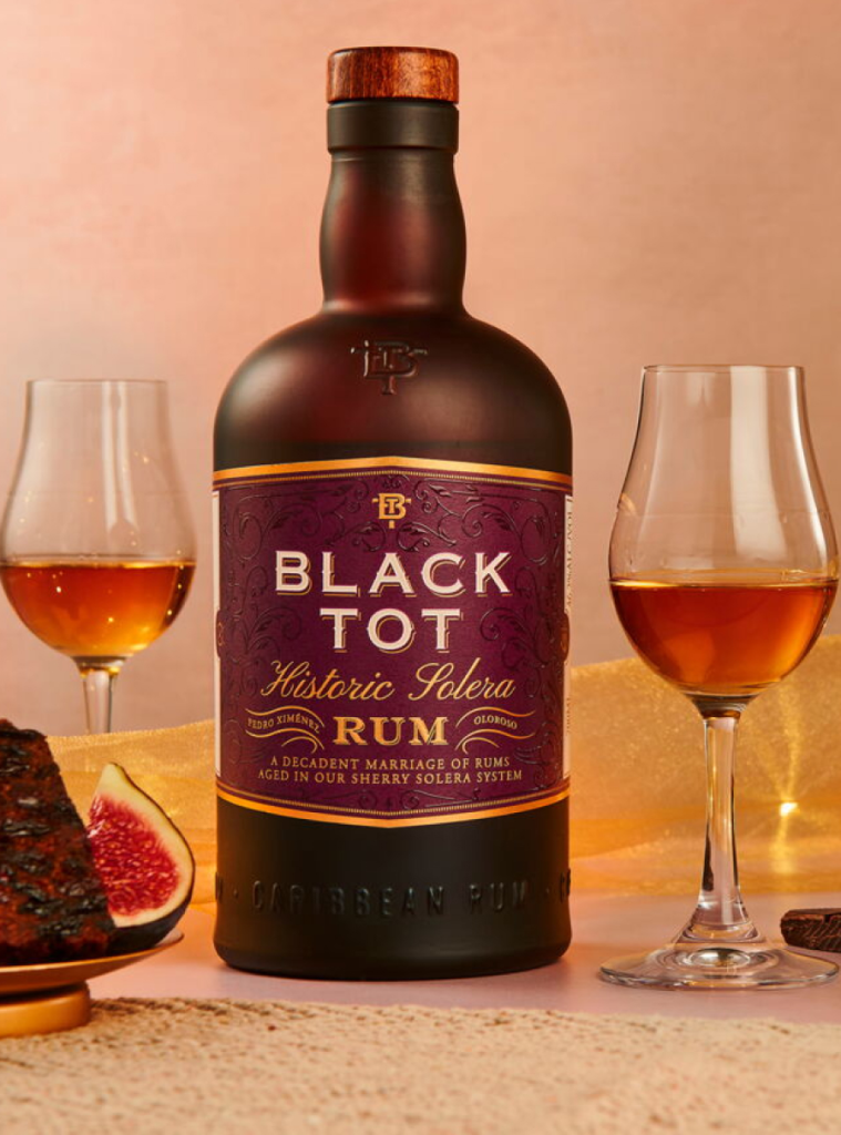 Primo piano del rum caraibico Black Tot Historic Solera posizionato tra due calici di vetro riempiti di distillato ambrato.