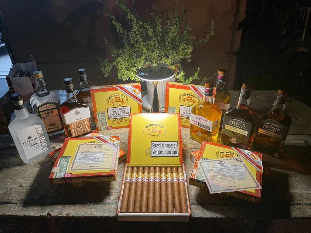 Scatole di sigari cubani Diplomaticos aperti sul tavolo accanto a diverse edizioni e bottiglie di Rhum Neisson tra cui Godinot.