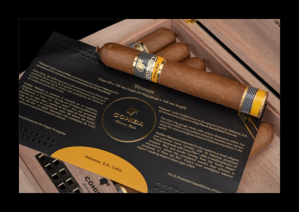 Primo piano del sigaro Cohiba Vistosos Vitola Dinoras adagiato sulla scheda tecnica informativa con dettagli di cepo e lunghezza.