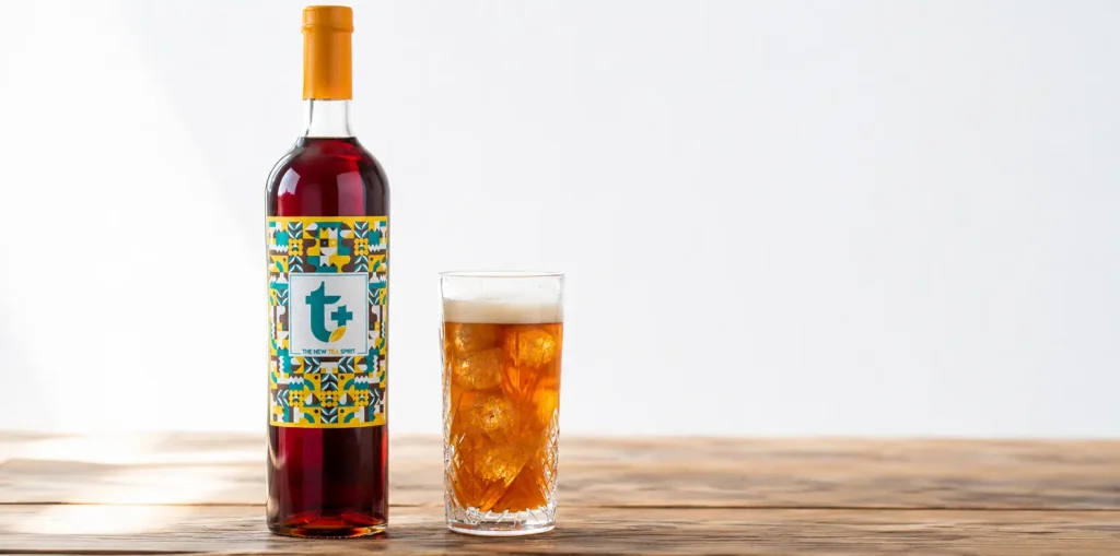 Bottiglia di liquore al tè T+ con bicchiere highball con ghiaccio appoggiati su un tavolo di legno