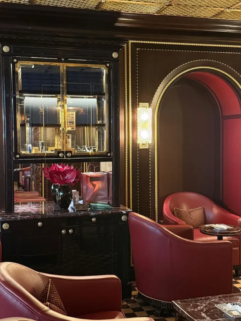 Elegante angolo della nuova Cigar Lounge del Ritz di Londra con poltrone in pelle rossa, pavimento a scacchi e mobile espositore classico in legno laccato nero lucido firmato DeART.