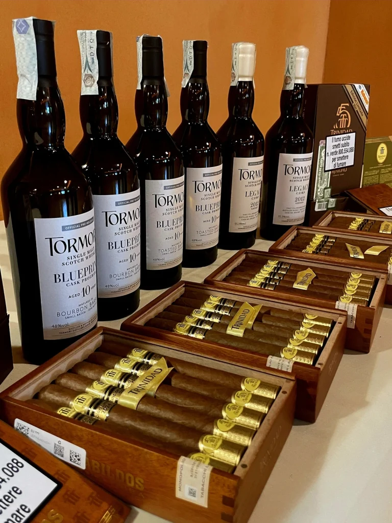 Line-up di bottiglie di Scotch Whisky Tormore Blueprint e Legacy esposte accanto alle scatole di sigari Trinidad Cabildos Edición Limitada.