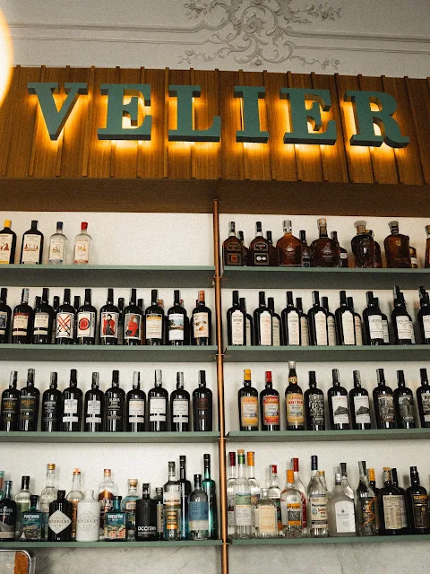 Grande parete con bottiglie rare di rum Caroni, gin e distillati sotto la scritta luminosa Velier